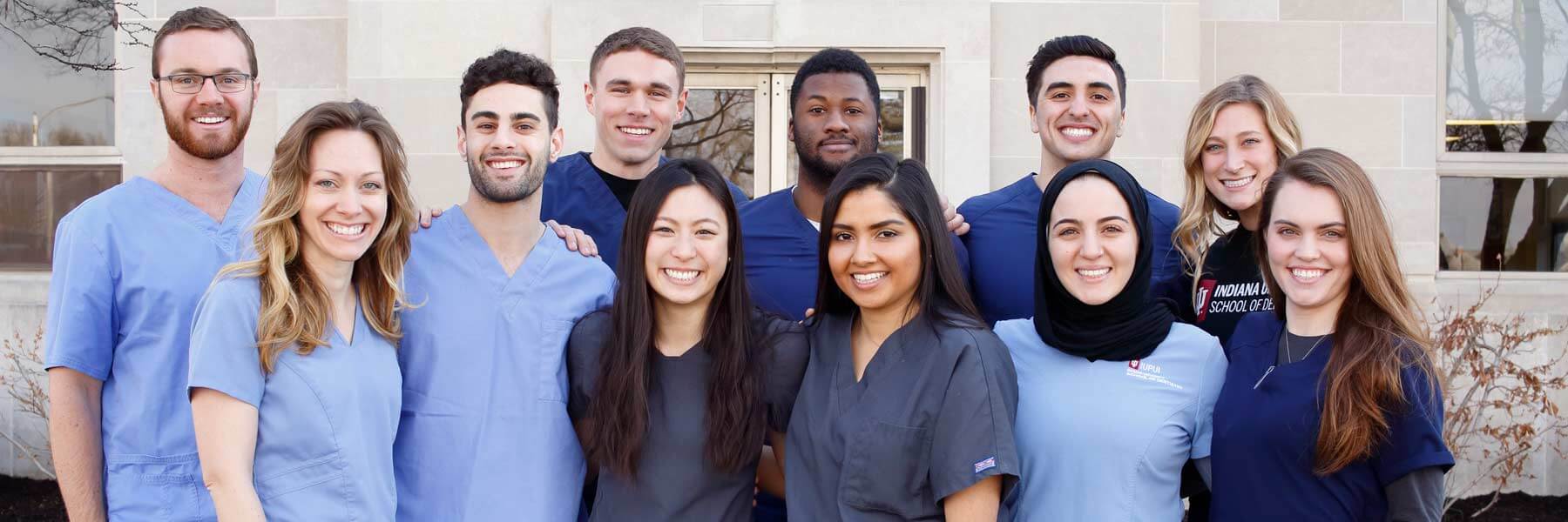 Dentistry students pose together and smile in their scrubs. 
