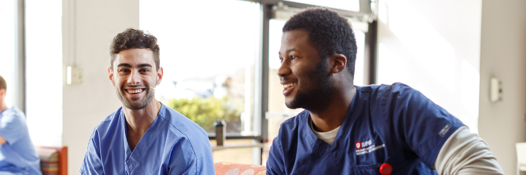 Two male dentistry students sit together and smile in a student common space.
